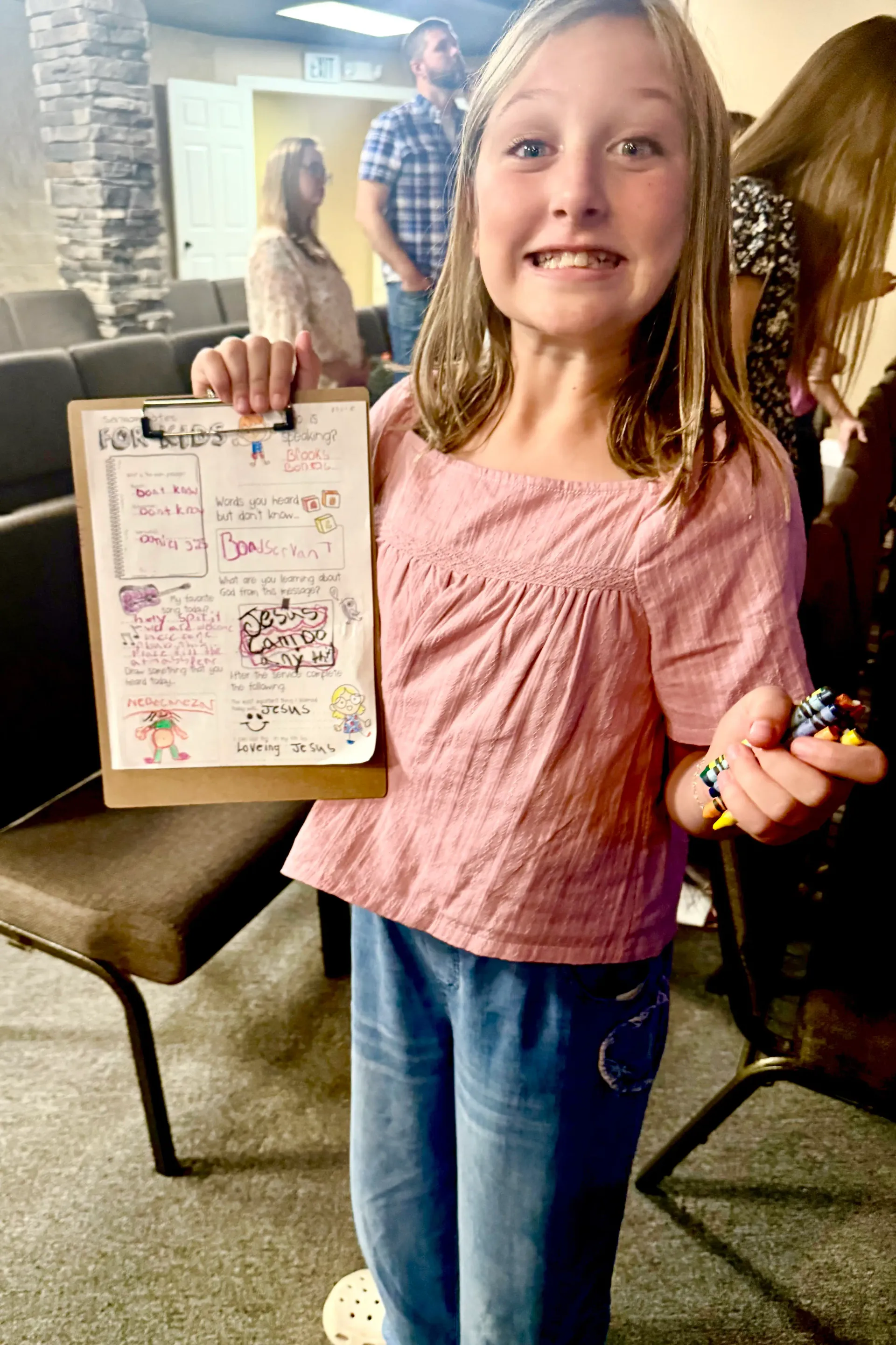 A child shares a handwritten drawing in a church family setting, with adults in the background